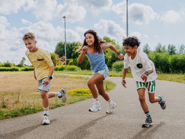 Drei Kinder laufen lachend auf einem Weg durch die Natur und erleben gemeinsam ein sommerliches Abenteuer.