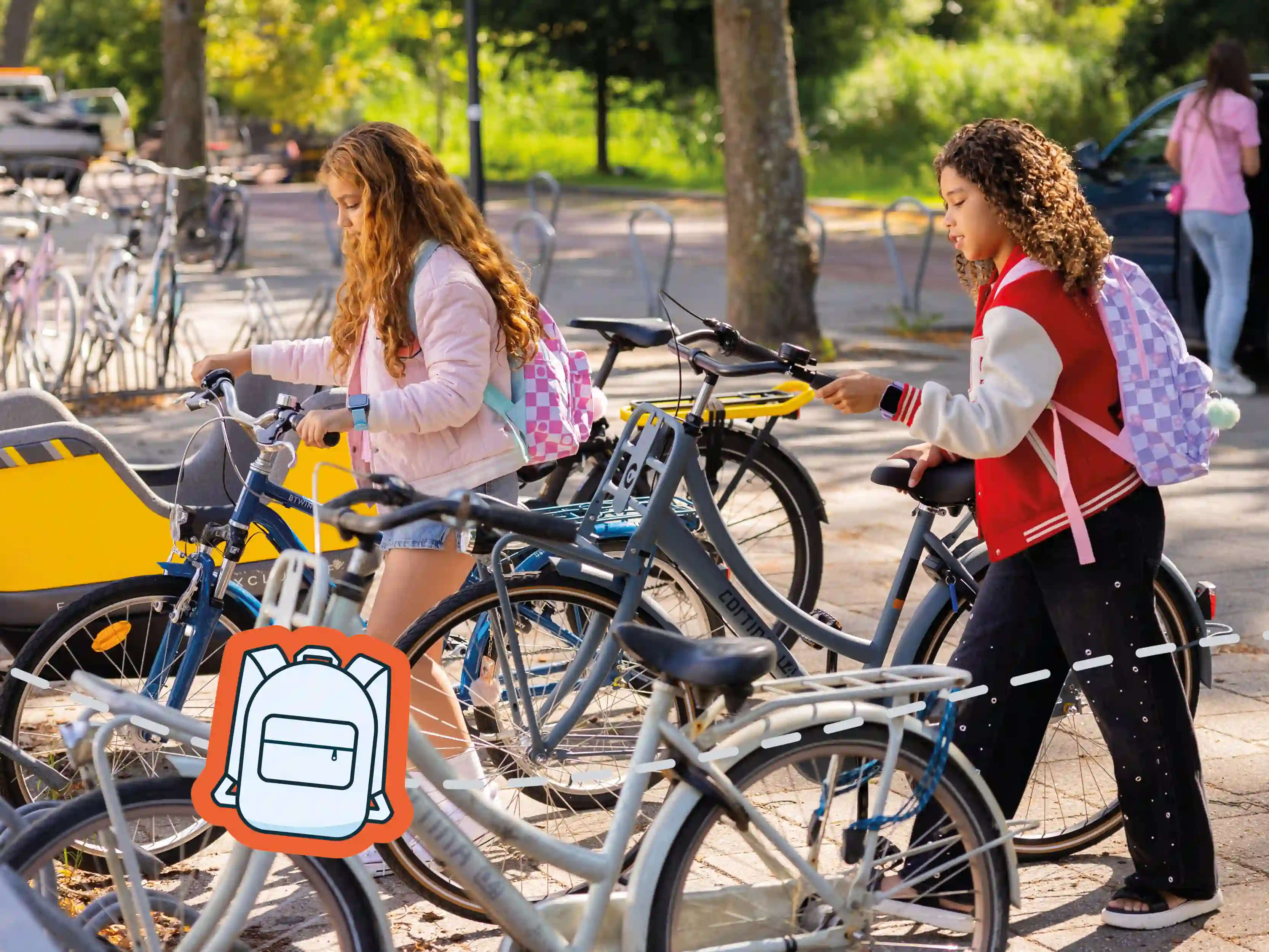 Zwei Kinder mit Rucksäcken und Kinder-Smartwatches schieben ihre Fahrräder an einem Fahrradständer vorbei.