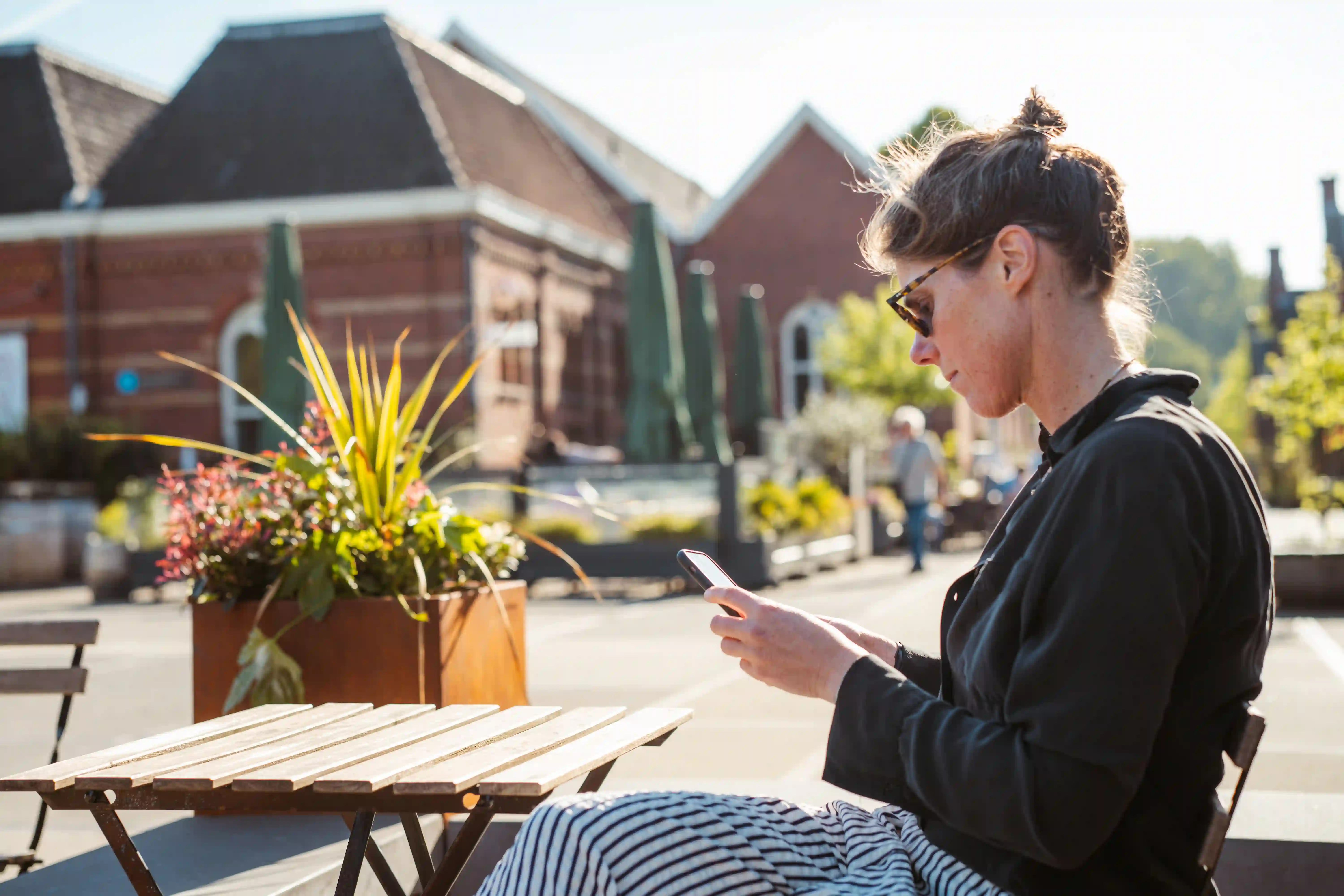 Frau sitzt draußen und nutzt ihr Smartphone auf einer sonnigen Terrasse.