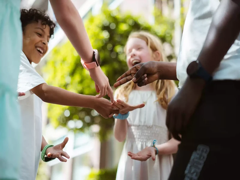 Kinder spielen draußen und vergleichen ihre Smartwatches lachend in einer Gruppe