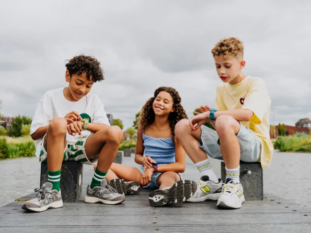 Drei Kinder tragen beim Spielen im Freien GPS-Uhren von one2track am Handgelenk.