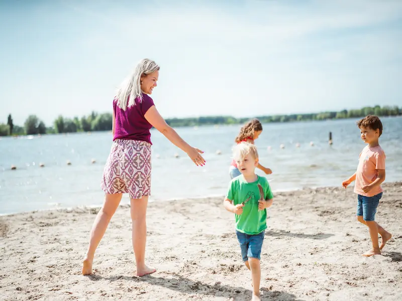 Mutter und Kinder spielen gemeinsam am Strand eines Badesees während eines Sommerurlaubs.