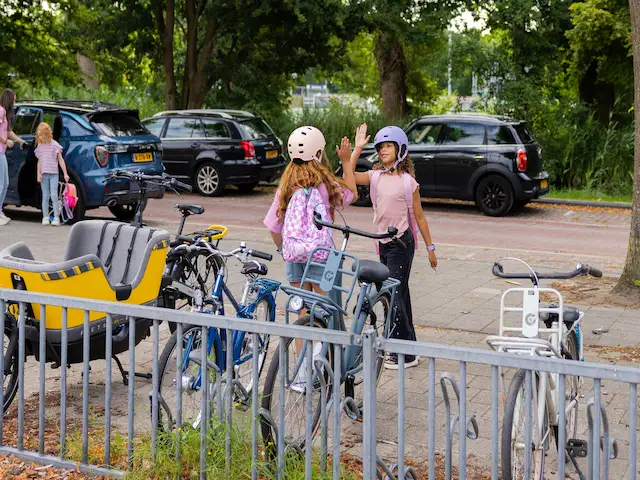 Zwei Kinder mit Fahrradhelmen begrüßen sich neben ihren Fahrrädern auf dem Schulhof.